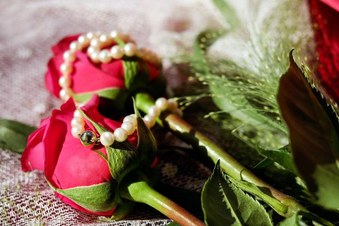 two red roses with a whte pearl necklace on top