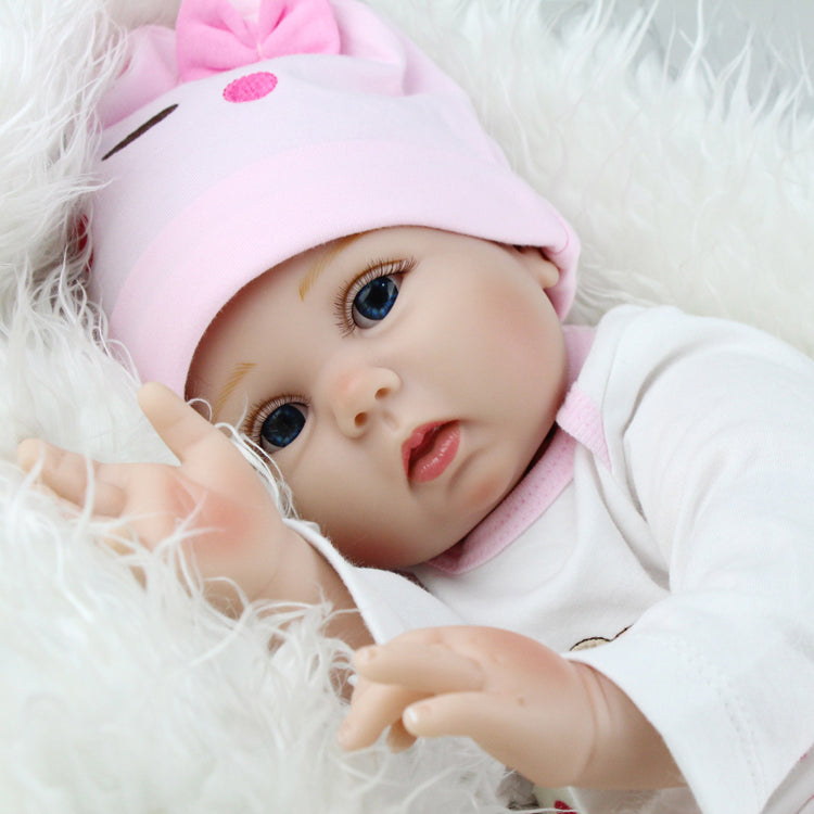 A NEWBORN BABY DOLL WEARING A PINK CAP, LYING DOWN